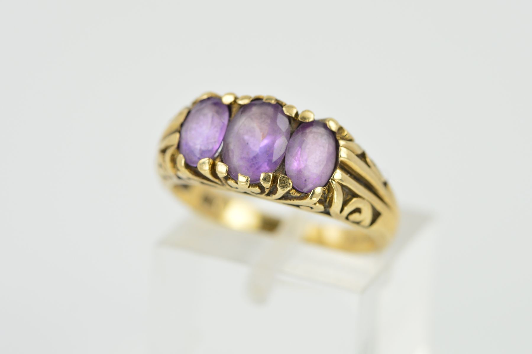 A LATE 20TH CENTURY 9CT GOLD THREE STONE AMETHYST RING, scroll engraved sides and shoulders, rings