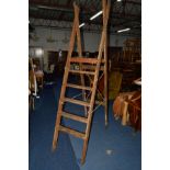 A WIDE WOODEN STEP LADDER, with casters to one side
