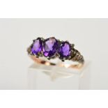AN AMETHYST RING, designed as three graduated oval amethysts within claw settings, to the shaped and