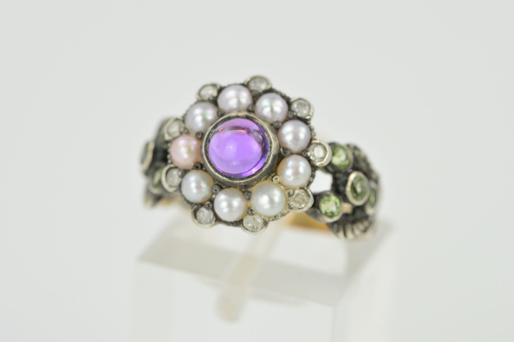 AN AMETHYST, SPLIT PEARL AND DIAMOND RING, designed as a central circular amethyst cabochon within a