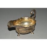 A GEORGE II SILVER SAUCEBOAT, of oval form, wavy rim, scroll over handle, engraved crest, on three