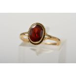 A 9CT GOLD GARNET RING, designed as an oval garnet within a collet setting to the rope twist
