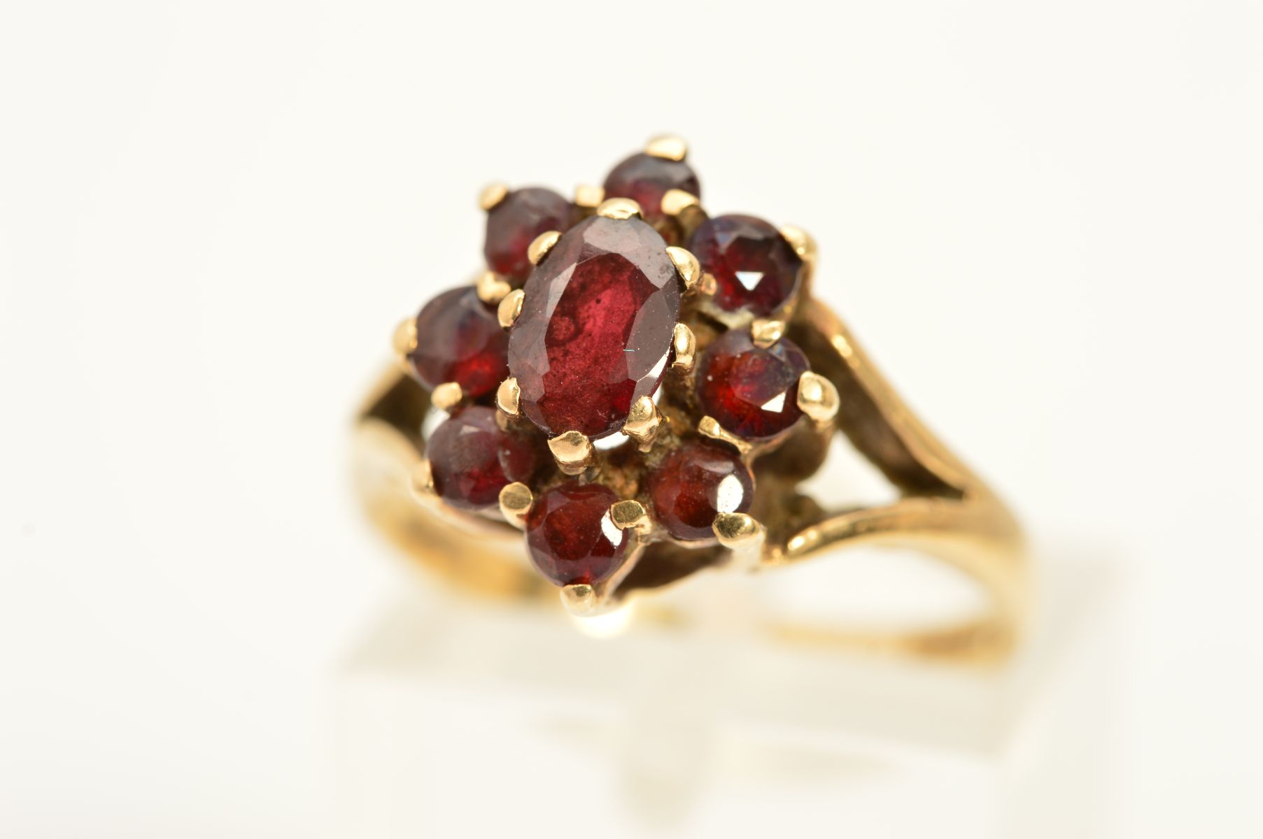 A 9CT GOLD GARNET CLUSTER RING, designed as a central oval garnet within a circular garnet surround,