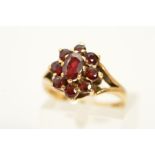 A 9CT GOLD GARNET CLUSTER RING, designed as a central oval garnet within a circular garnet surround,
