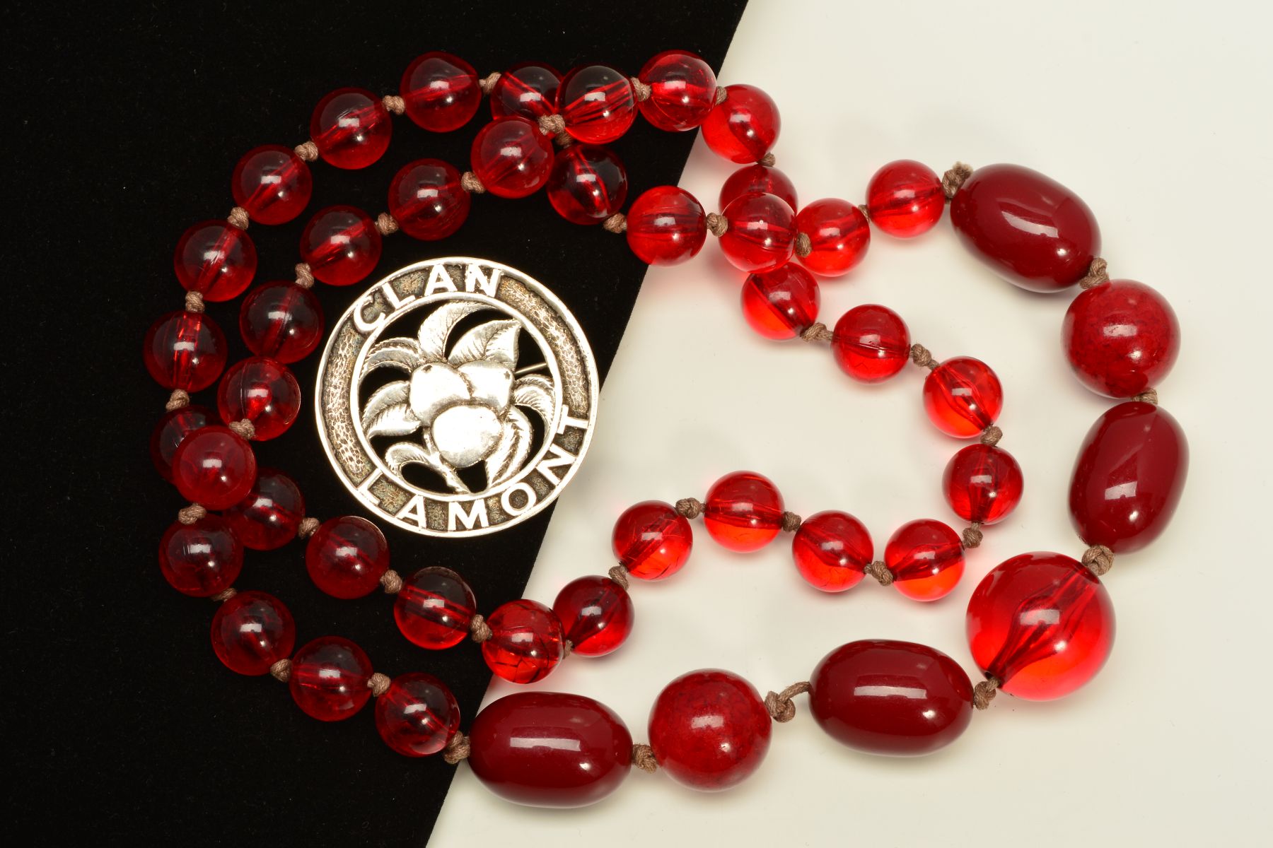 A RED PASTIC BEAD NECKLACE AND A SCOTTISH BROOCH, the necklace with spherical and barrel shape