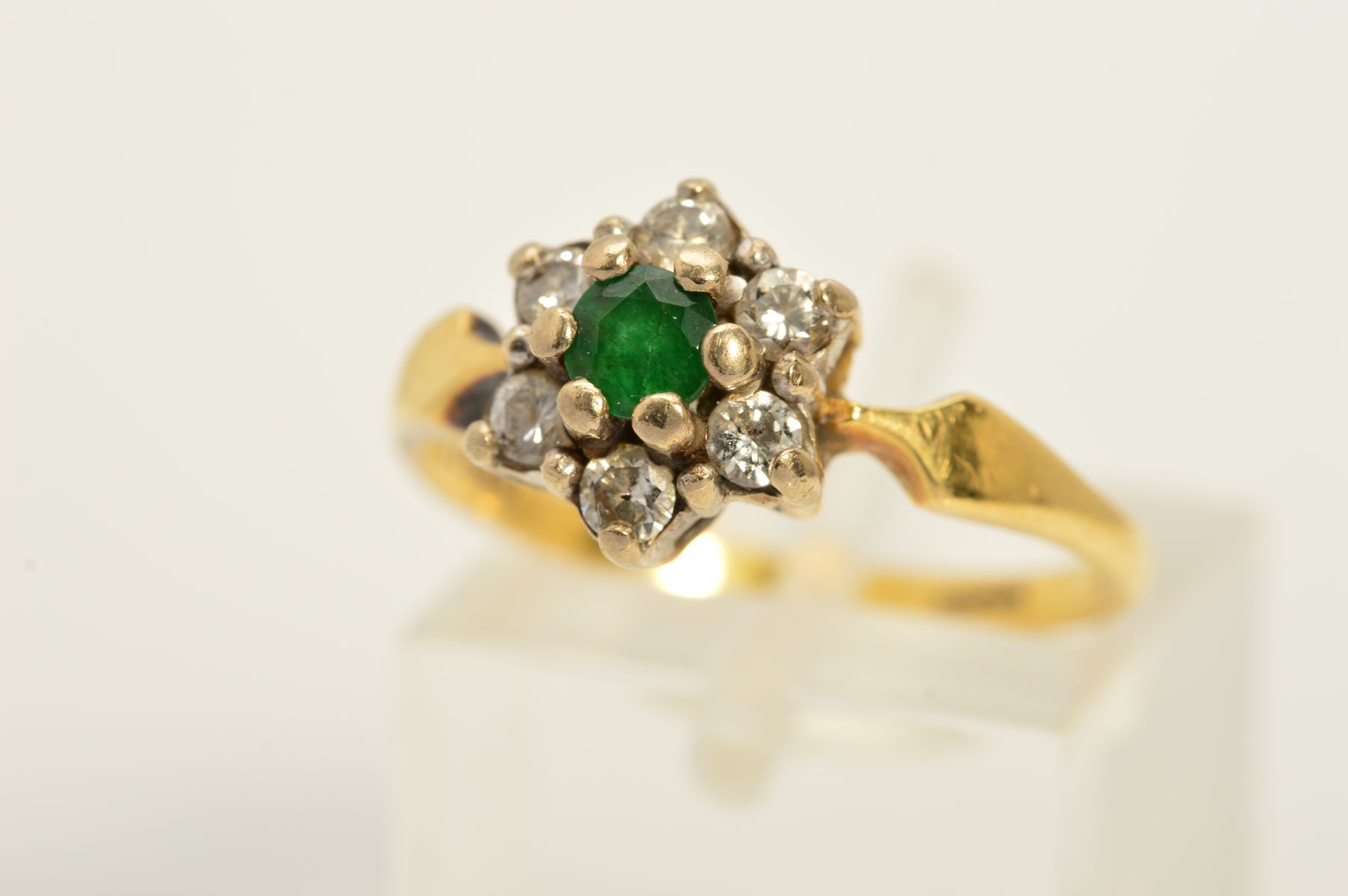 AN 18CT GOLD EMERALD AND DIAMOND CLUSTER RING, the central circular emerald within a brilliant cut