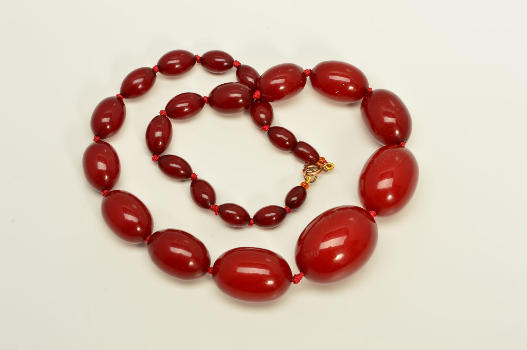 A RED PLASTIC BEAD NECKLACE, designed as graduated barrel shape beads measuring 11mm to 36mm to