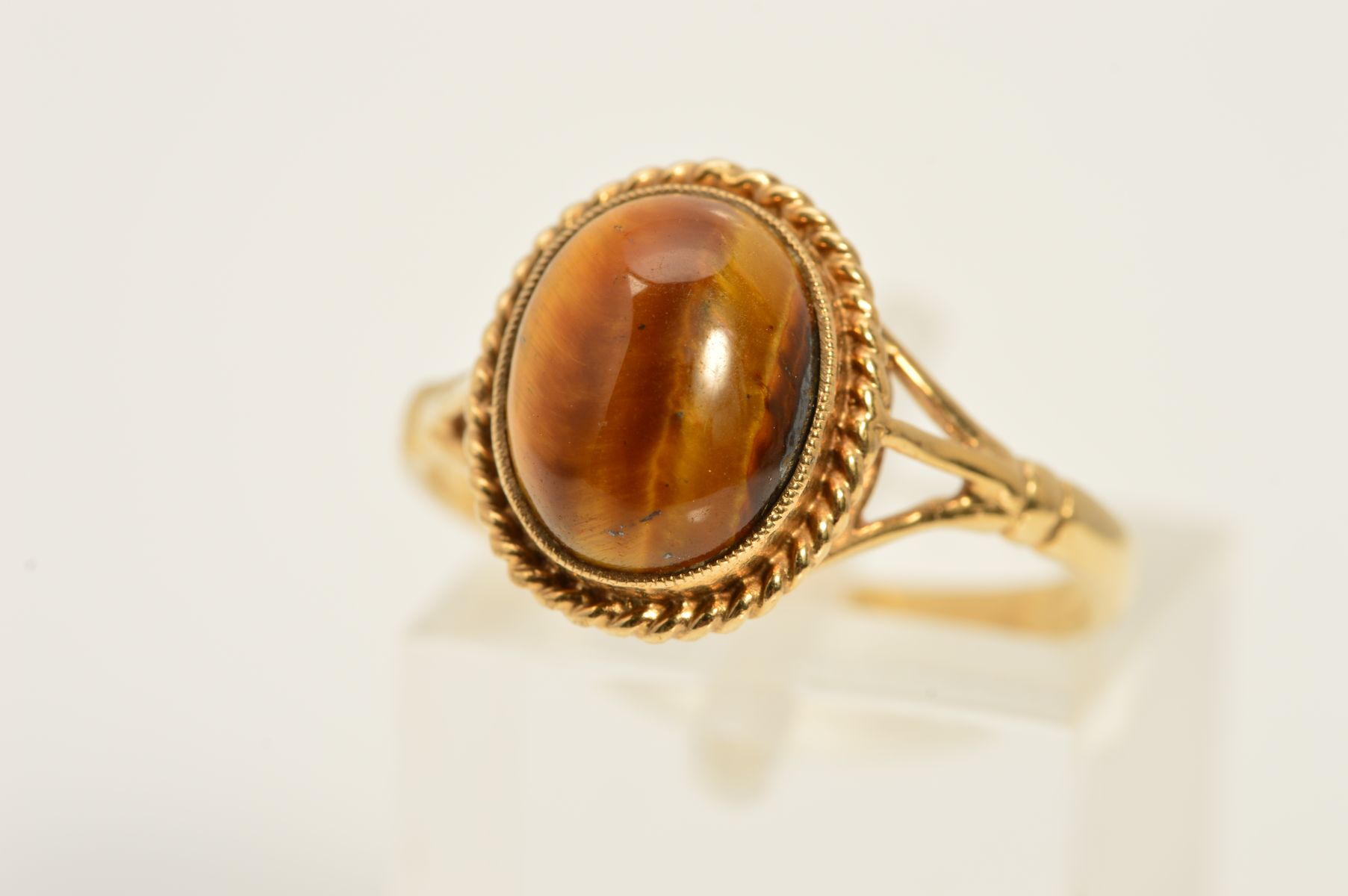 A 9CT GOLD TIGER'S EYE RING, designed as an oval tiger's eye cabochon within a rope twist surround