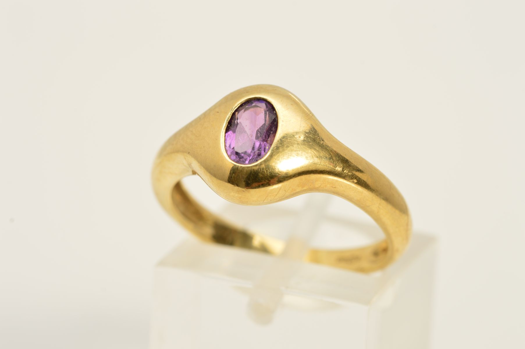 A 9CT GOLD AMETHYST RING, designed as an oval, flush set amethyst, to the plain band, with 9ct