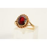A 9CT GOLD GARNET RING, designed as an oval garnet within a rope twist surround to the bifurcated