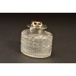 AN EDWARDIAN SILVER MOUNTED OVAL GLASS INKWELL, the hinged cover set with a Cairngorm (brown