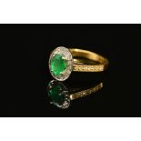 A MODERN 18CT GOLD EMERALD AND DIAMOND HALO CLUSTER STYLE RING, with diamond set shoulders,