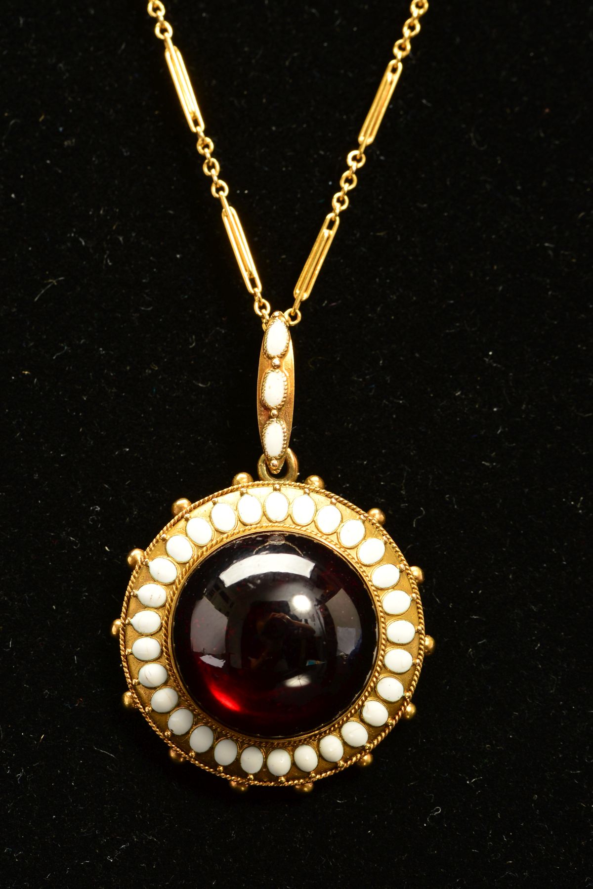 A MID VICTORIAN GOLD GARNET AND WHITE ENAMEL PENDANT, centring on a large cabochon circular garnet