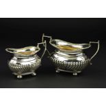 AN EDWARDIAN SILVER OVAL CREAM JUG AND SUGAR BOWL, gadrooned rims and part reeded bodies, on