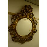 A GILT WOOD HEAVY FOLIATE FRAMED CIRCULAR WALL MIRROR, with scrolled decoration and plaque above,