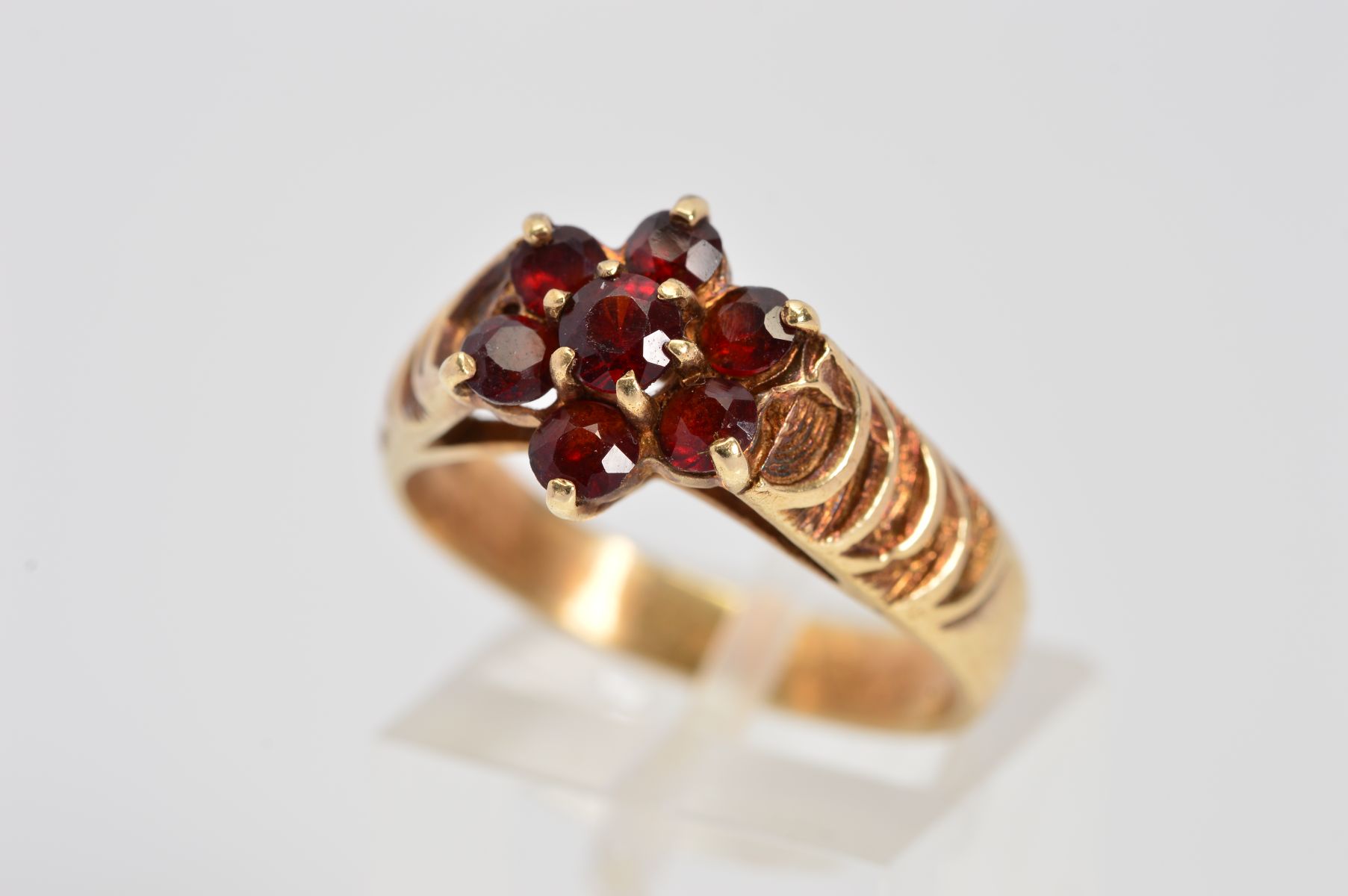 A 9CT GOLD GARNET CLUSTER RING designed as a floral cluster of seven circular garnets to the