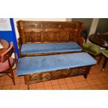 A REPRODUCTION CARVED OAK HALL SETTLE, having various carved panels with a blue upholstered seat,