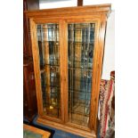 A REPRODUCTION GOLDEN OAK GLAZED TWO DOOR DISPLAY CABINET having a mirror back and four glass