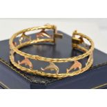 A MODERN THREE COLOUR GOLD DOLPHIN BANGLE, a hinged oval bangle of open work design measuring
