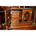 AN EDWARDIAN OAK DOUBLE GLAZED DOOR SMOKERS CABINET with a hinged top and three various drawers,