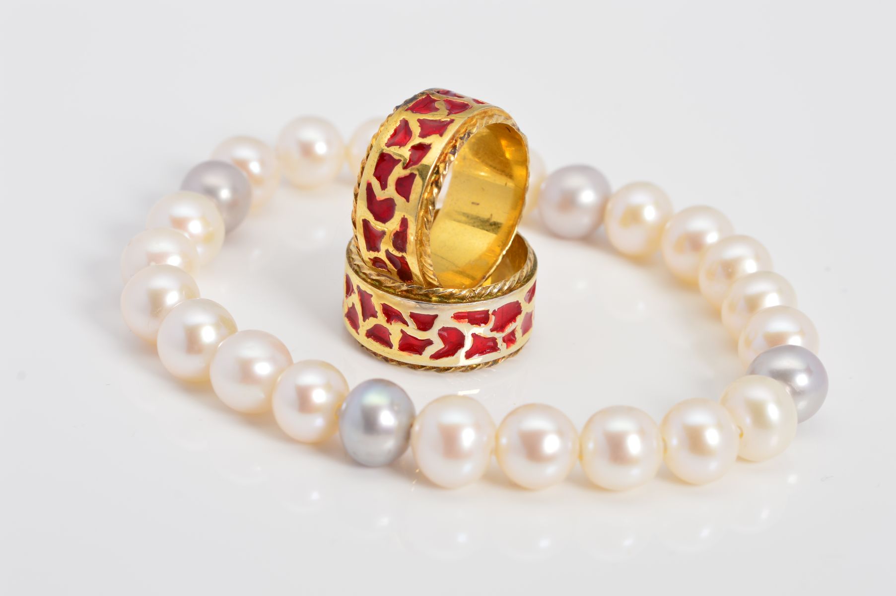 TWO MODERN SILVER GILT RED ENAMEL BAND RINGS and a freshwater grey and white elastic bracelet,