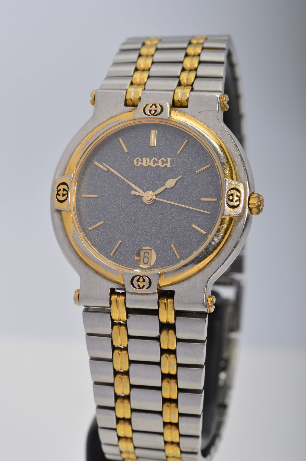 A GUCCI STAINLESS STEEL WRISTWATCH, the dark grey face with baton hour markers, date dial and gold