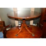 A REPRODUCTION MAHOGANY CIRCULAR TOPPED DINING TABLE on an oak base with four legs with brass caps
