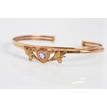A MODERN AMETHYST TORC BANGLE, centering on a heart shaped amethyst within a foliate surround,