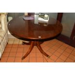 A REPRODUCTION MAHOGANY CIRCULAR TOPPED DINING TABLE on an oak base with four legs with brass caps