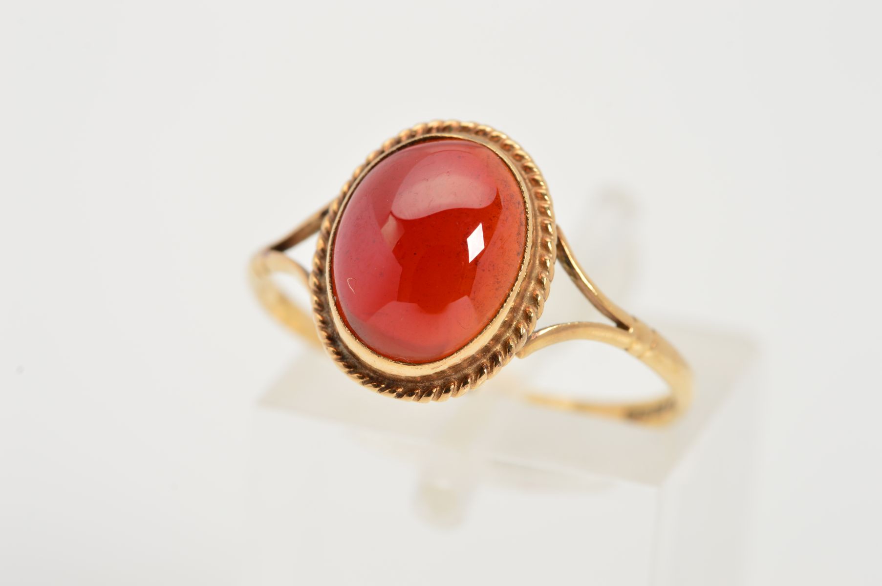 A 9CT GOLD GEM RING, designed as a central oval red gem cabochon within a collet setting and rope