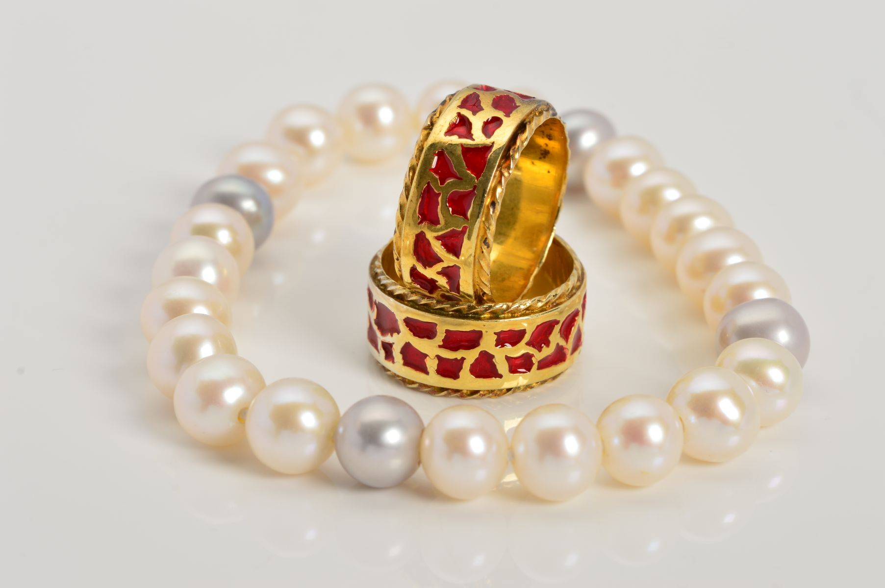 TWO MODERN SILVER GILT RED ENAMEL BAND RINGS and a freshwater grey and white elastic bracelet,