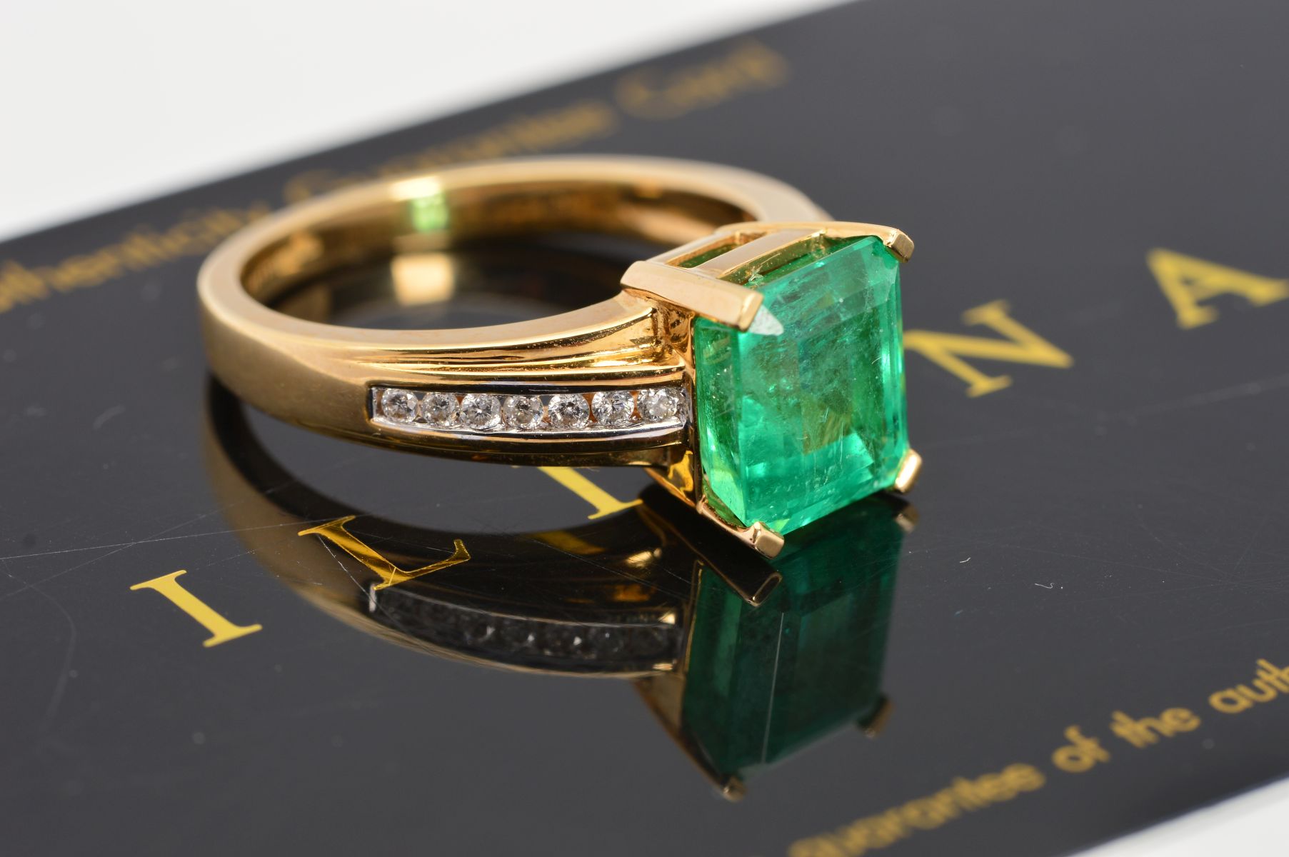 AN 18CT GOLD EMERALD AND DIAMOND RING, the central rectangular emerald within a four claw setting to
