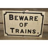 A CAST IRON BEWARE OF TRAINS SIGN, raised black lettering and edge on white background, length