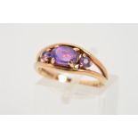 A 9CT GOLD AMETHYST RING, designed as a central oval amethyst flanked by circular amethysts to the