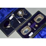 A CASED PAIR OF EDWARDIAN SILVER SALTS, of circular form on three sinuous scrolling supports, blue