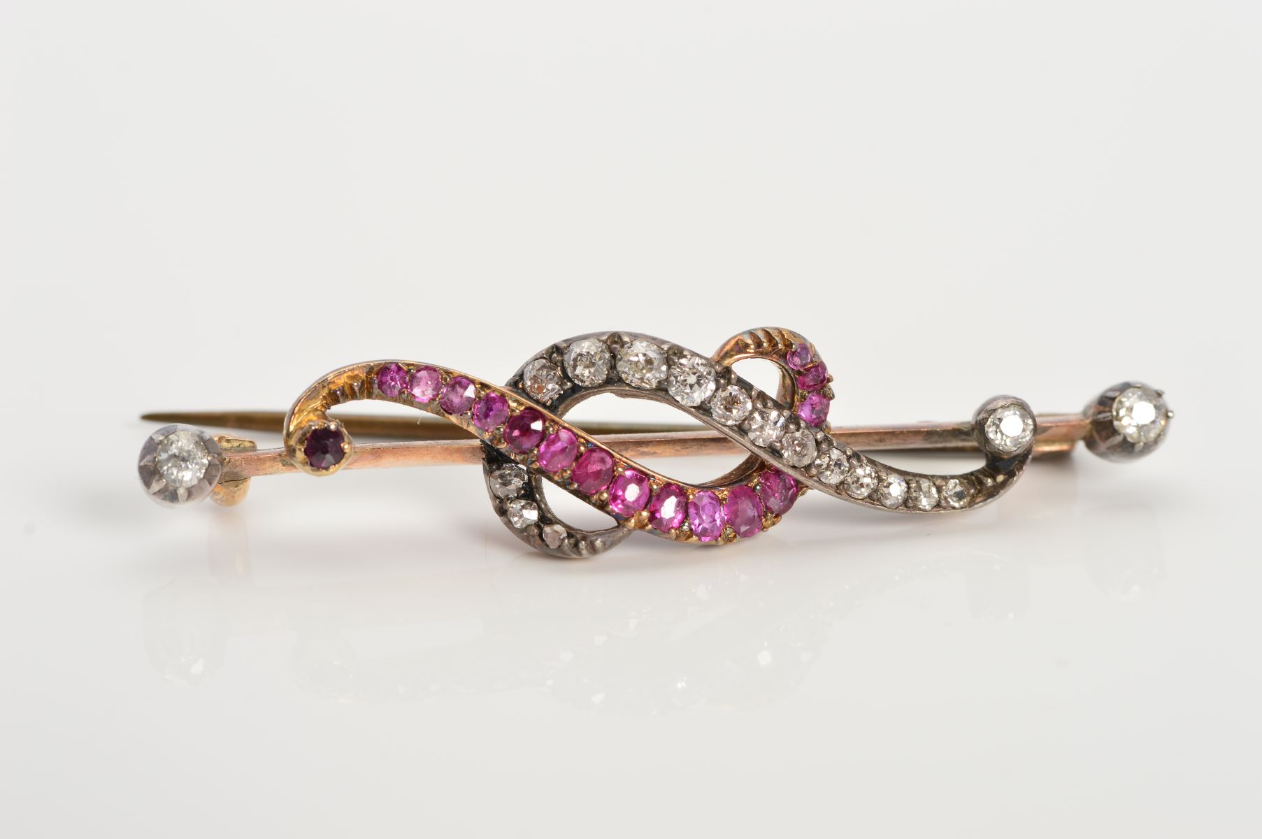 AN EARLY 20TH CENTURY RUBY AND DIAMOND BAR BROOCH, designed as two over lapping curved lines, one