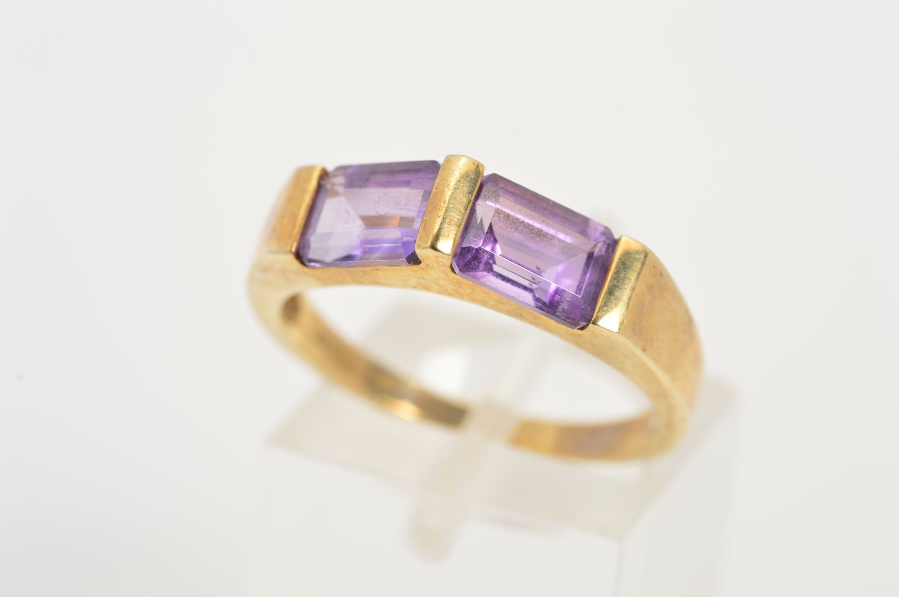 A 9CT GOLD AMETHYST RING, designed as two rectangular amethysts horizontally set at an upward angle,