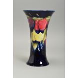 A WILLIAM MOORCROFT PLUM WISTERIA DESIGN VASE, of conical form with flared rims, dark blue ground,