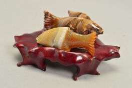 TWO CARVED FISH ORNAMENTS ON WOODEN BASE, in jasper and banded agate, measuring approximately 7cm,