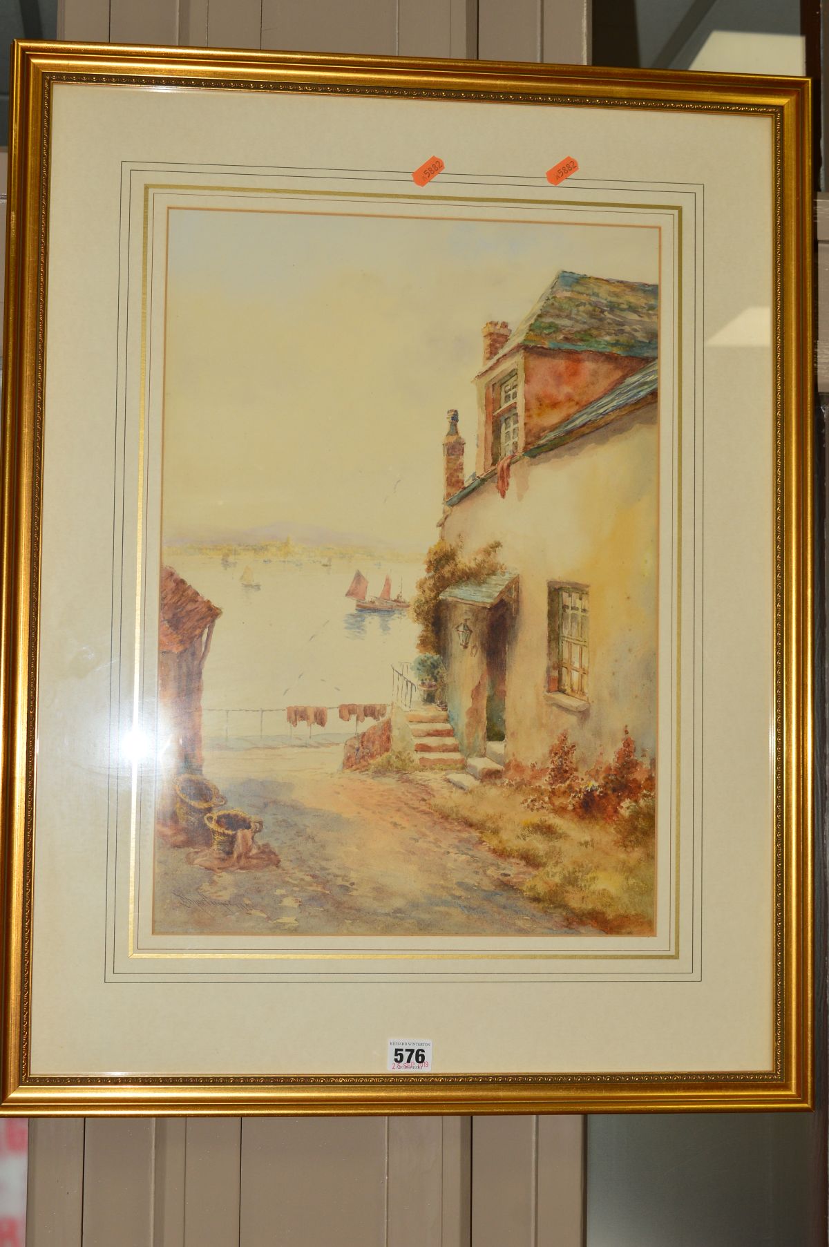 A WATERCOLOUR OF A COTTAGE OVERLOOKING A HARBOUR, indistinctly signed, dated 1921, mounted, framed