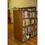 AN OAK VENEERED DOUBLE SIDED ROLLING BOOKCASE, with eight adjustable shelves and wheels,