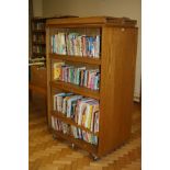AN OAK VENEERED DOUBLE SIDED ROLLING BOOKCASE, with eight adjustable shelves and wheels,