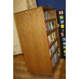 AN OAK VENEERED DOUBLE SIDED ROLLING BOOKCASE, with eight adjustable shelves and wheels,