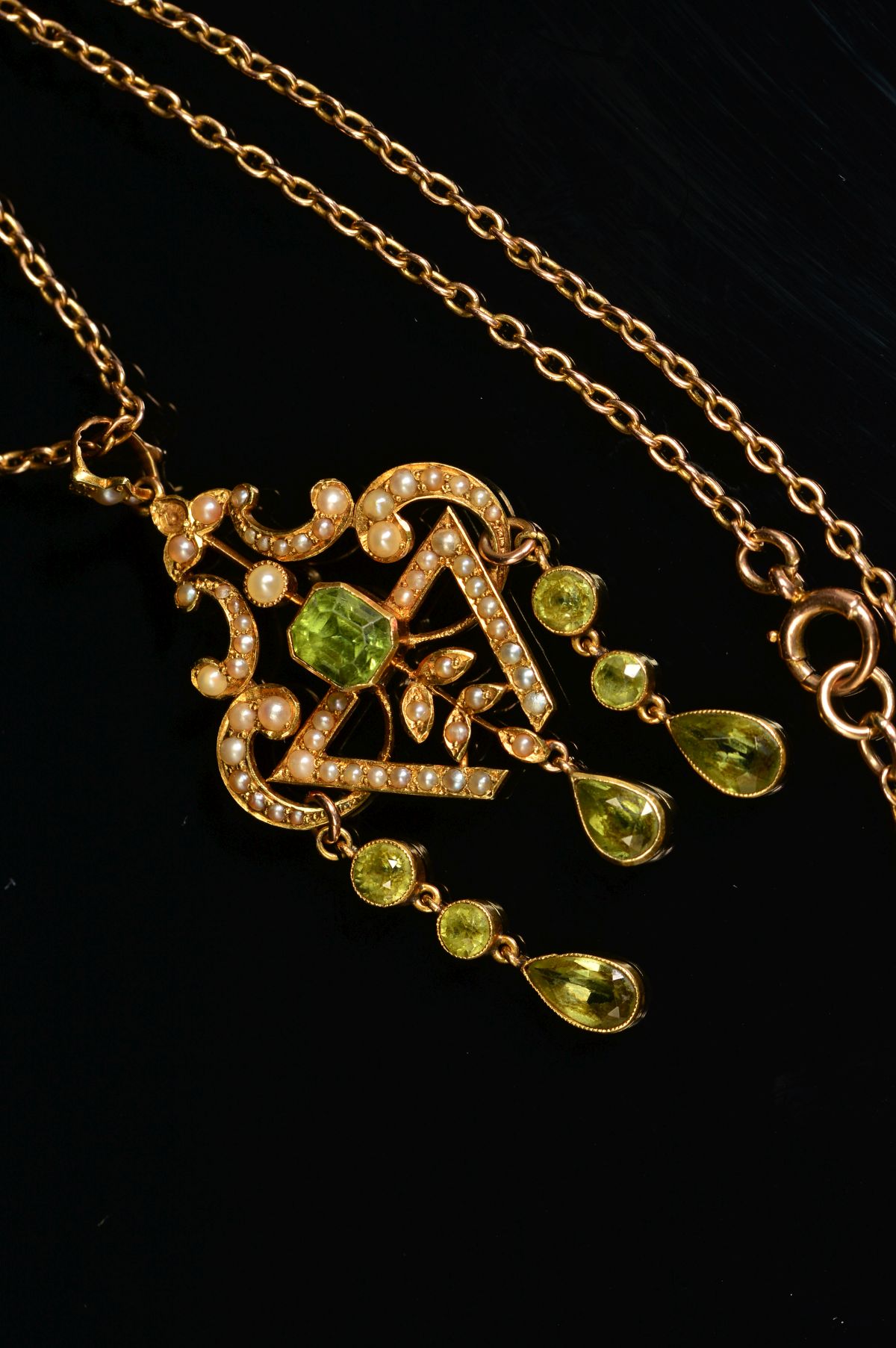 AN EARLY 20TH CENTURY PERIDOT AND SEED PEARL PENDANT, a fancy open scroll work design, suspending