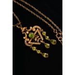 AN EARLY 20TH CENTURY PERIDOT AND SEED PEARL PENDANT, a fancy open scroll work design, suspending