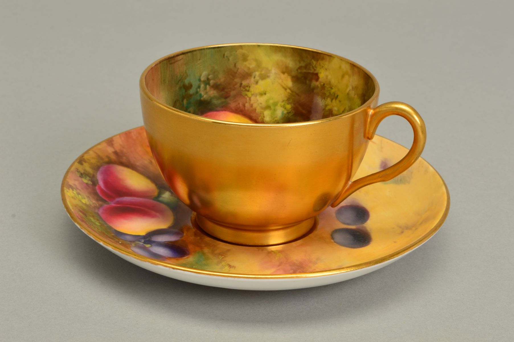 A ROYAL WORCESTER FRUIT STUDY TEACUP AND SAUCER, the exterior of the cup gilded, the interior