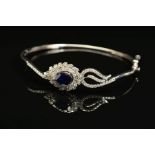 AN OVAL HINGED SAPPHIRE AND DIAMOND BANGLE, centring on a pear cut blue sapphire which is