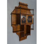 An Edwardian oak and ebonised wall cabinet, the shaped back, with an arrangement of shelves on