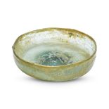 A small Islamic greenish glass dish, 9th-10th century, with uneven vertical walls and lop-sided