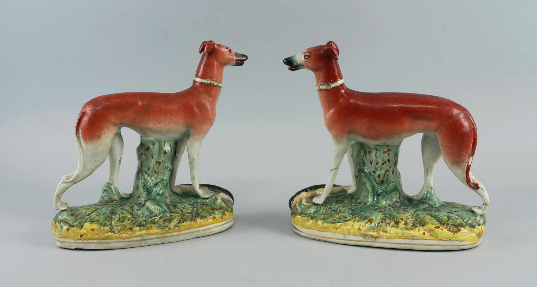 A pair of Staffordshire greyhounds, 19th century, modelled standing on oval naturally modelled bases